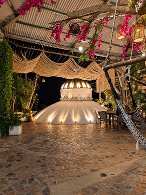 A covered outdoor area with a stone floor, a central dome structure, and hanging wicker lamps.