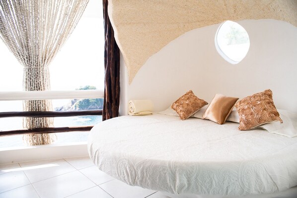 A bedroom with a large bed, a window with curtains, and a view of the outdoors. - Hotel Pasión de Luna (San Pedro Pochutla)