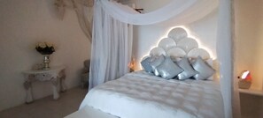 Ein Bett mit Baldachin, ein Nachttisch mit einer Vase und eine Wand mit einer Dekoration.