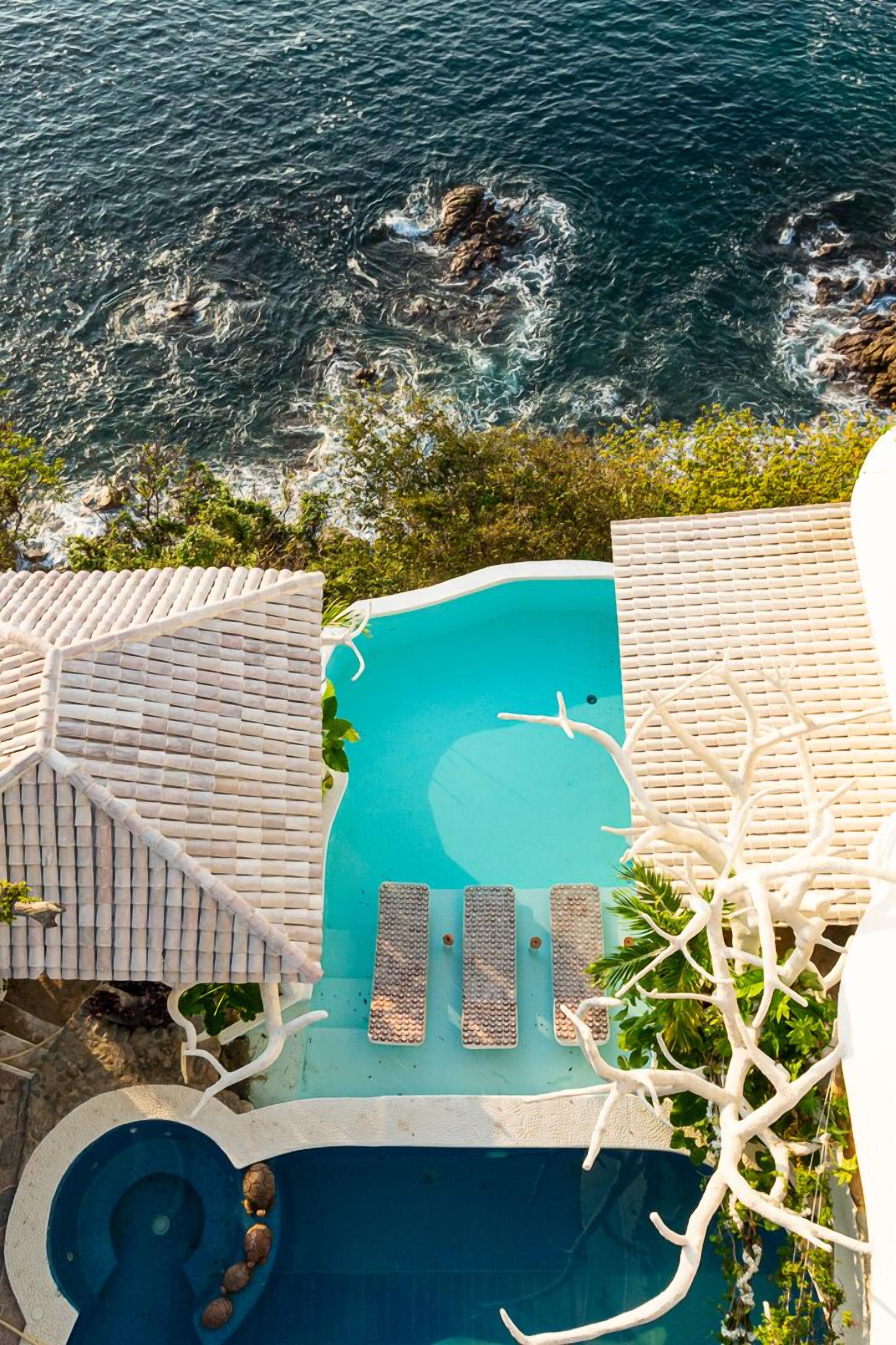 A pool with a view of the ocean, surrounded by lounge chairs and a small hot tub.