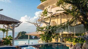 A poolside area with a clear view of the sea, a pergola, and a multi-level building with greenery.