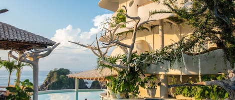 Un espace aménagé au bord de la piscine offrant une vue dégagée sur la mer, un pergolas et un bâtiment à plusieurs niveaux agrémenté de verdure.