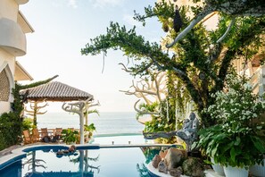 Ein Poolbereich mit Meerblick, einem Kiosk und üppiger Bepflanzung.