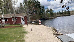 Une propriété au bord du lac, avec un bâtiment rouge, une plage de sable et une jetée qui s’avance dans l’eau.