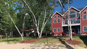 Une maison rouge à deux étages, avec un garage apparent et un arbre dans le jardin.