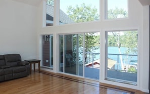 Amplia sala de estar con ventanas grandes, un sofá gris y una pequeña mesa.