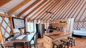 Een gezellige joert met een houten interieur, een eethoek, keuken en een bed.