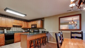 A kitchen with wooden cabinets, a central island with stools, a dining table, and a chandelier.