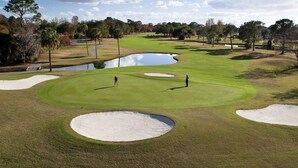 Um campo de golfe com bunkers de areia, lago e árvores ao fundo.