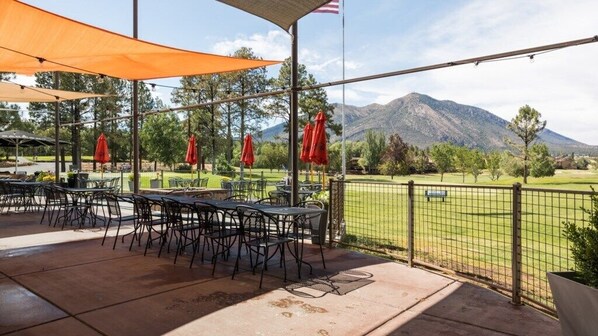 Un patio al aire libre con mesas y sillas, vista a un campo de golf y una montaña al fondo.