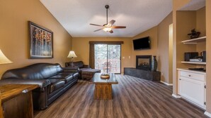 Un salon avec un canapé en cuir, une table basse, un ventilateur de plafond et un téléviseur fixé au mur.
