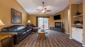 A living room with a leather sofa, a coffee table, a ceiling fan, and a TV mounted on the wall.