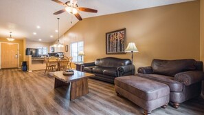 A spacious living room with a dark brown leather sofa, a wooden coffee table, and a ceiling fan.