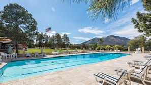 A swimming pool with lounge chairs, an American flag, and mountains in the background.