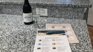 A kitchen counter with a bottle of wine, a glass, and a sign listing house rules. - Keowee Key ~ Cozy Condo ~ Golf Course View - Amenities (Salem)