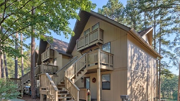A two-story wooden cabin with a balcony on the upper floor, surrounded by trees. - Keowee Key ~ Cozy Condo ~ Golf Course View - Amenities (Salem)
