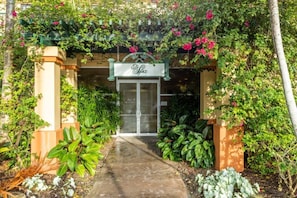 Enter a serene oasis beneath a lush greenery-adorned archway, leading to a clean and modern hotel entrance.