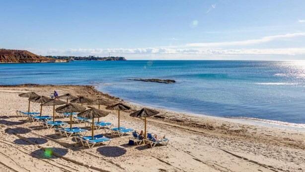 Une plage avec des chaises longues et des parasols, un ciel dégagé et une mer calme.