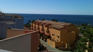 Un hôtel en bord de mer doté de nombreux balcons donnant sur la mer, avec une façade en terre cuite et une terrasse sur le toit.