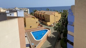 Un quartier résidentiel doté d’une piscine entourée d’immeubles, offrant une vue dégagée sur la mer et agrémenté de palmiers.