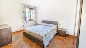 Ein Schlafzimmer mit einem Bett, zwei Nachttischen, einer Kommode und einem Fenster mit Vorhängen.