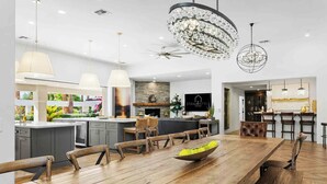 Une cuisine moderne dotée d’un grand îlot central, de luminaires suspendus et d’un coin repas avec des tables et des chaises en bois.