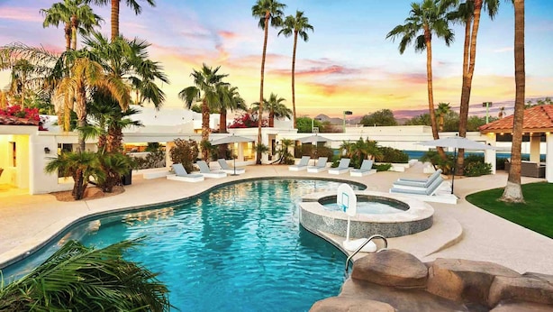 Un espace piscine doté de chaises longues, de palmiers et d’un jacuzzi.