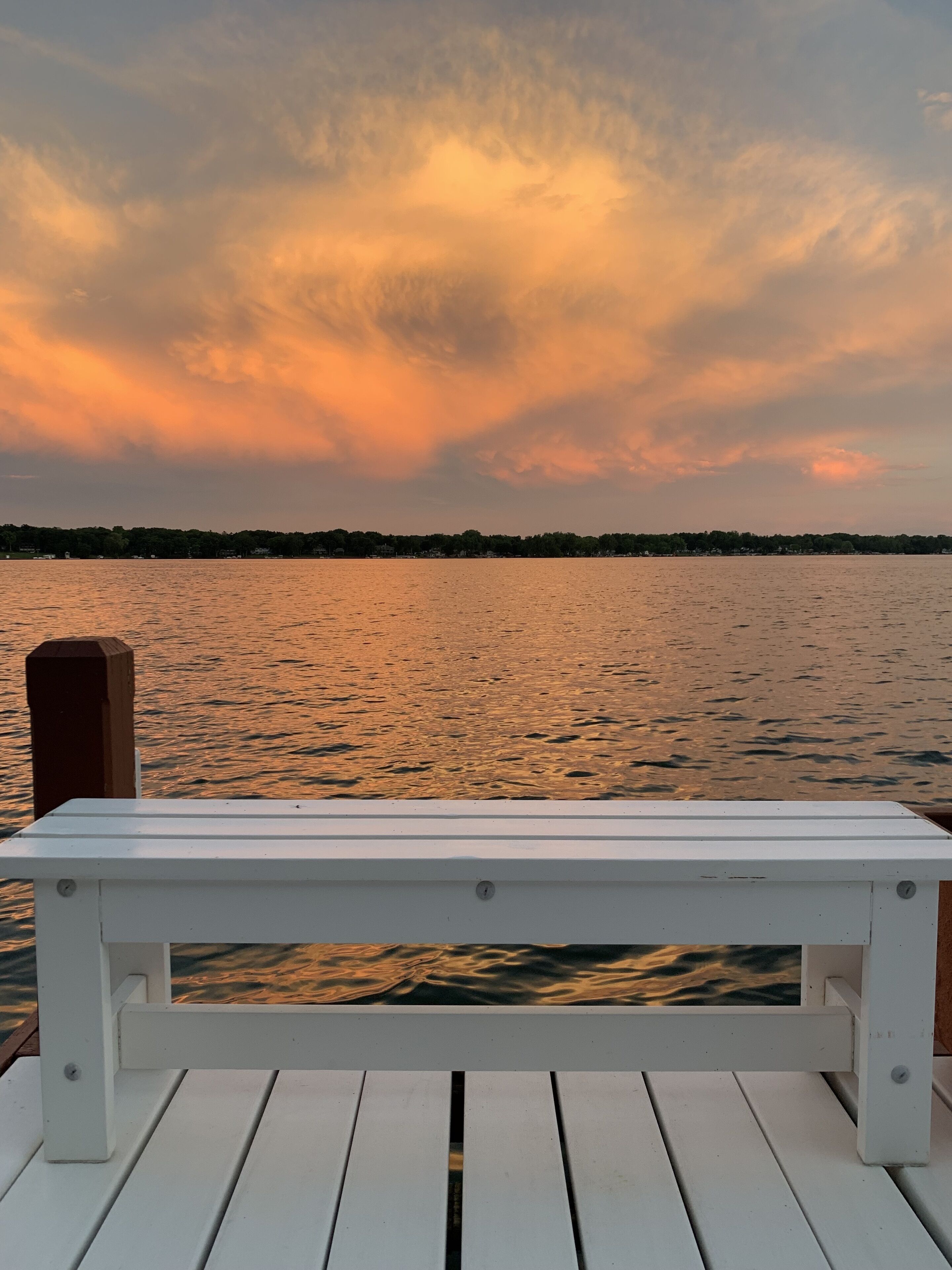 A white wooden bench on a dock overlooking a body of water with a sunset sky.