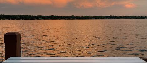 A white wooden bench on a dock overlooking a body of water with a sunset sky.