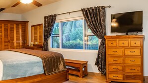 Un dormitorio con cama, cómoda de madera, televisor, lámpara y cortinas.