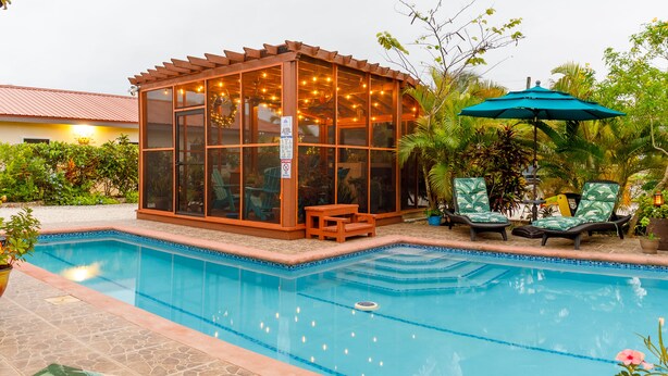 Un área de piscina con una cabaña de vidrio, sillas de descanso y una estatua tiki.