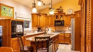 Una cocina con gabinetes de madera, encimeras de granito, horno empotrado, microondas, refrigerador y un comedor con taburetes de bar.