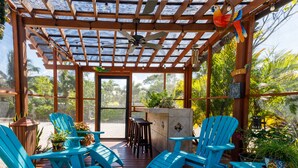 Un espacio de estar al aire libre techado, con sillas y mesa de madera, rodeado de follaje y vistas del exterior.