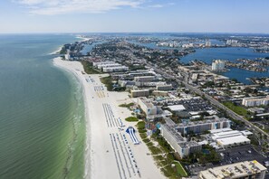 An aerial view of a coastal city with a long beachfront, a marina, and dense urban development.