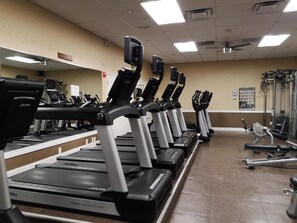 A row of treadmills in a gym with a mirrored wall and various exercise equipment.