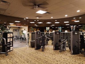 A gym with exercise equipment, a patterned carpet, and a ceiling fan.