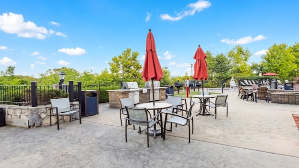 An outdoor patio with stone seating, red umbrellas, and a barbecue area.