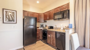 A compact kitchen with wooden cabinets, a black refrigerator, a microwave, a stove, and a dishwasher.