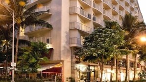 A multi-story hotel with balconies, palm trees, and a street view.