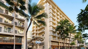 A multi-story hotel with balconies, palm trees, and storefronts.