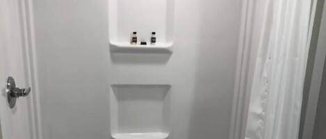 Un baño con cabina de ducha blanca, un inodoro y un estante pequeño con artículos de aseo.