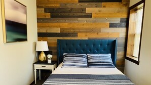 A bedroom with a bed, a nightstand, a lamp, and a wall with a wooden plank design. - Rockwood Resort Motel (Lake Ozark)