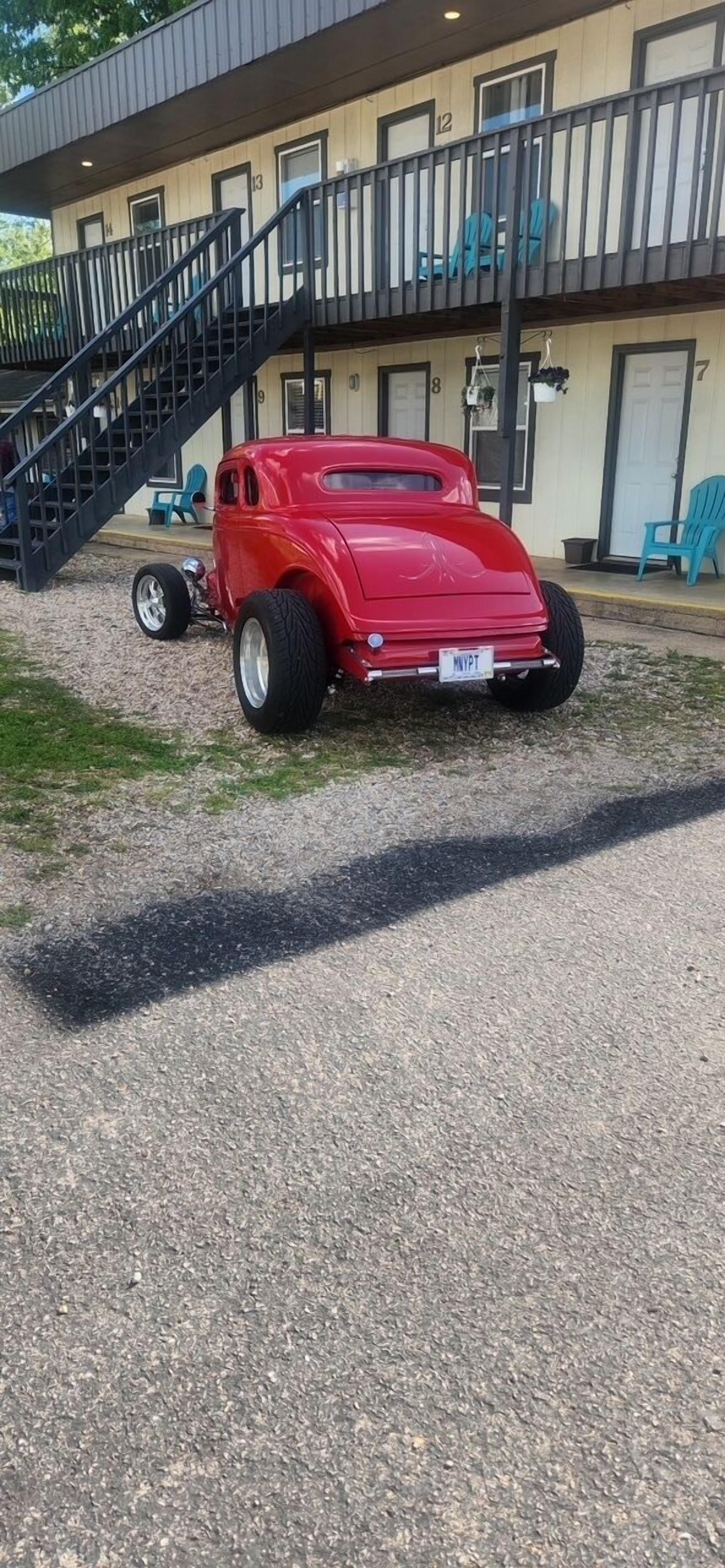 A red vintage car parked in front of a building with a staircase leading to a balcony.