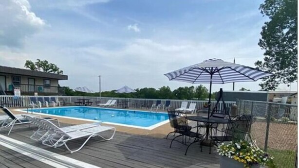 A poolside area with a wooden deck, lounge chairs, a table with chairs, and a potted plant. - Rockwood Resort Motel (Lake Ozark)