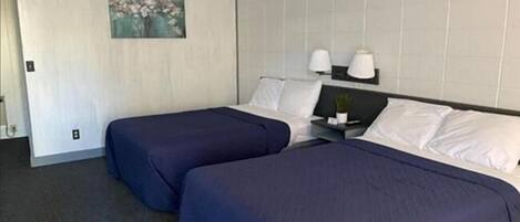 Habitación de hotel con dos camas individuales, una mesita de noche pequeña con lámpara y un cuadro en la pared.