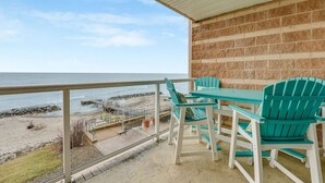 A balcony with a view of the beach and ocean, featuring a table and chairs. - Lakefront Condo, Balcony, Pool, Beach, Wineries (Geneva)