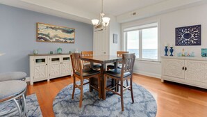 A dining area with a table and chairs, a chandelier, a painting, and a view of the ocean. - Lakefront Condo, Balcony, Pool, Beach, Wineries (Geneva)