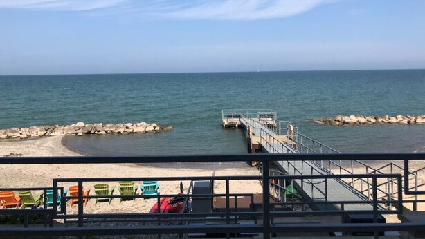 A beach view with a pier extending into the water, a sandy beach, and a railing in the foreground. - Lakefront Condo, Balcony, Pool, Beach, Wineries (Geneva)