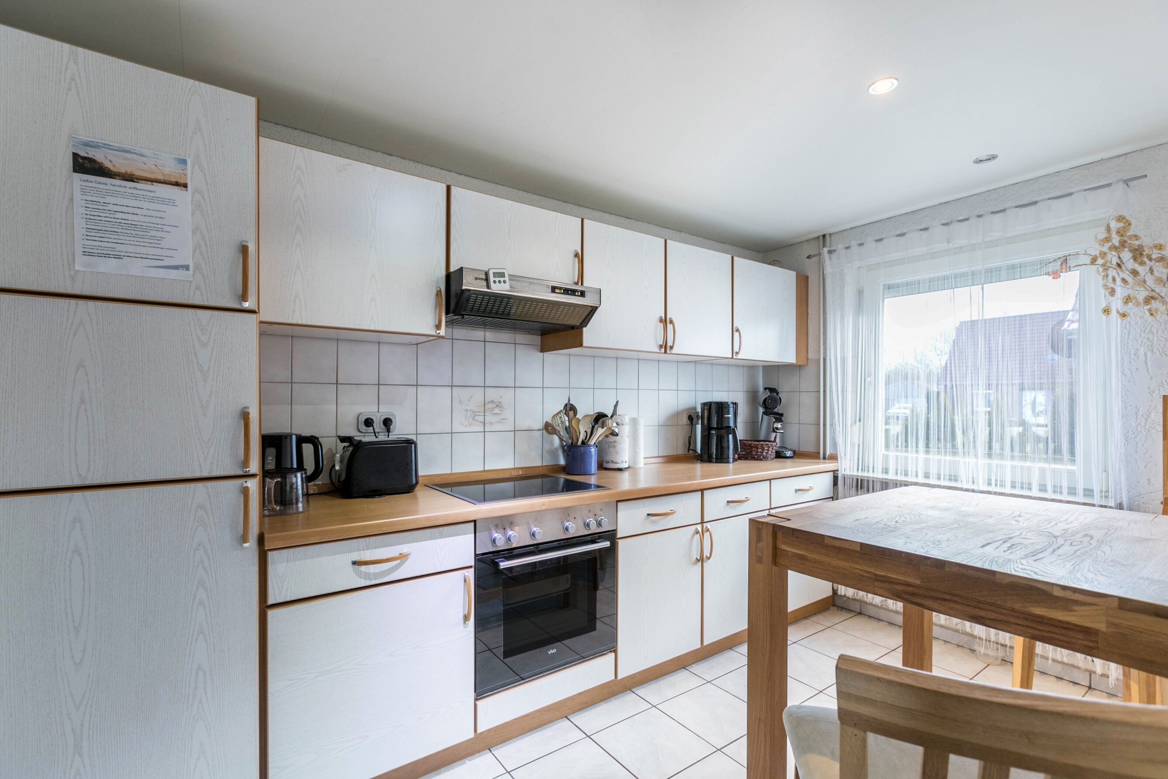 Eine moderne Küche mit weißen Schränken, einer Holztischplatte, einem eingebauten Backofen und einem Esstisch mit Stühlen.