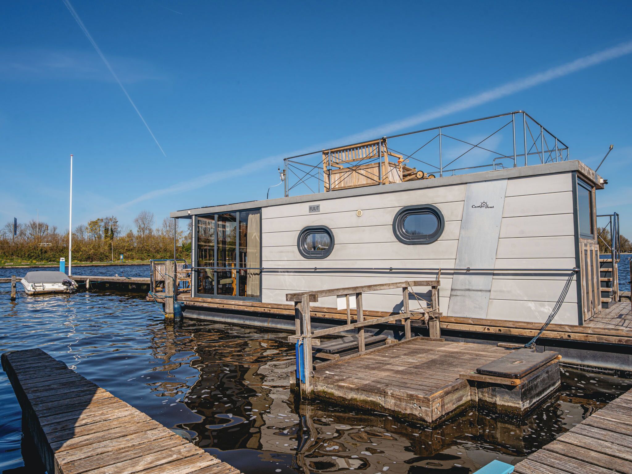A stationary houseboat docked at a pier with a covered deck area and a small outdoor seating space.